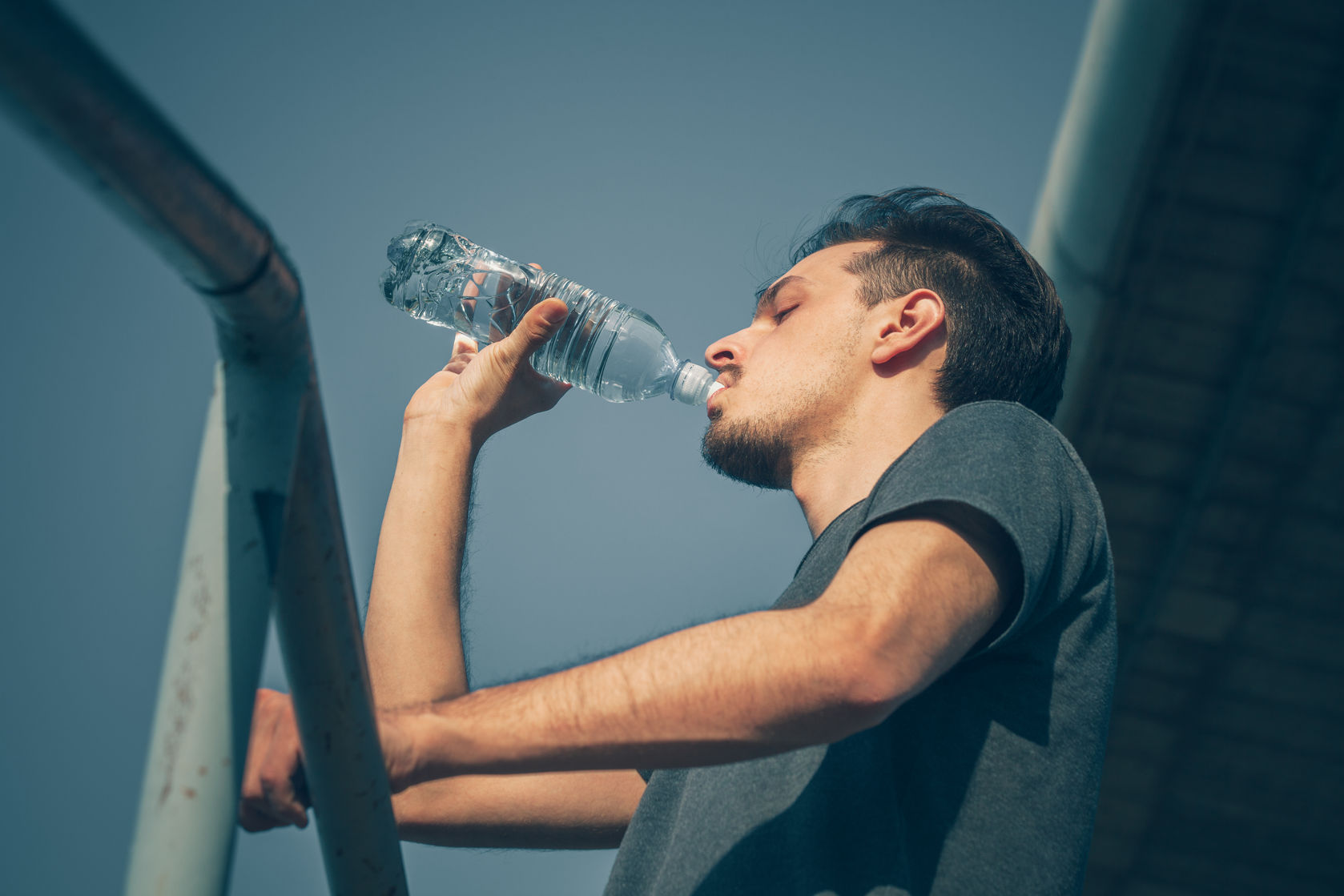 74892796 - young man drinking water after running in the city  hot summer day closeup shot from below